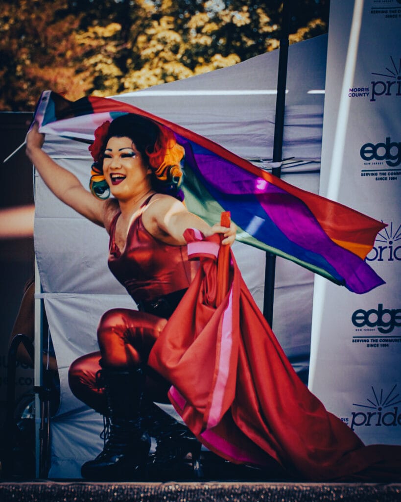 Performer Mimi Sashimi in a red outfit waves a rainbow pride flag during a performance at Morris County Pride.