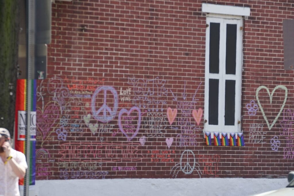 Colorful chalk drawings and messages including hearts, peace signs, and Pride slogans cover a brick wall in New Hope.