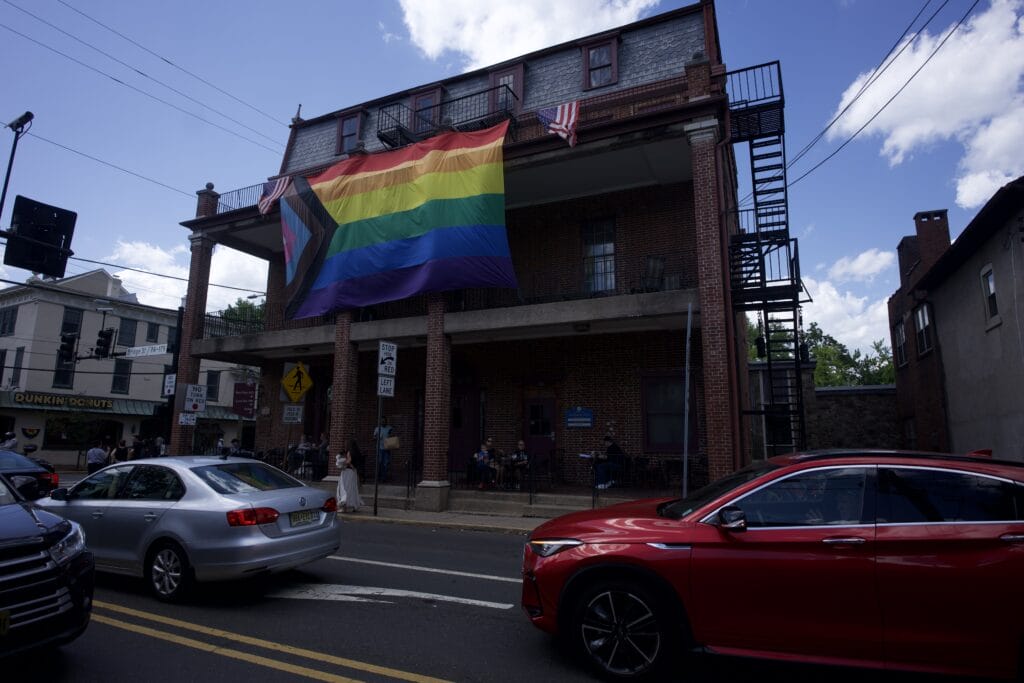 Large Progress Pride flag hangs from a balcony on a brick building in New Hope, Pennsylvania during Pride.