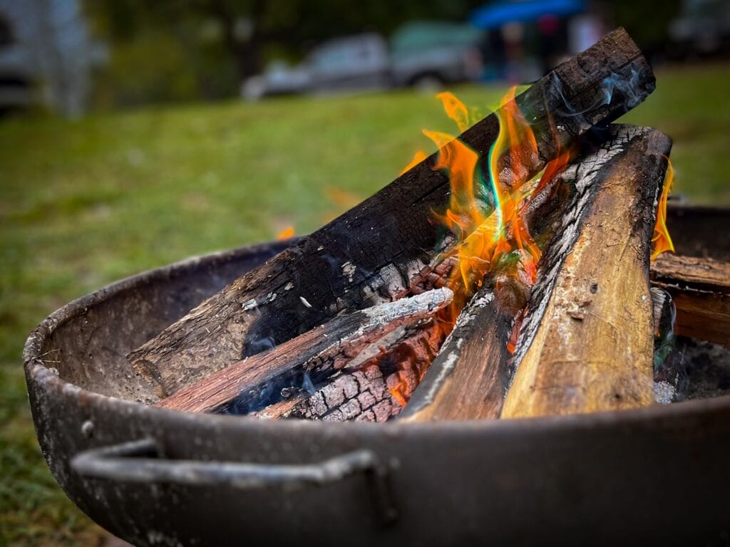 Campfire burning inside a metal fire pit at a wooded campsite during Lezapalooza.