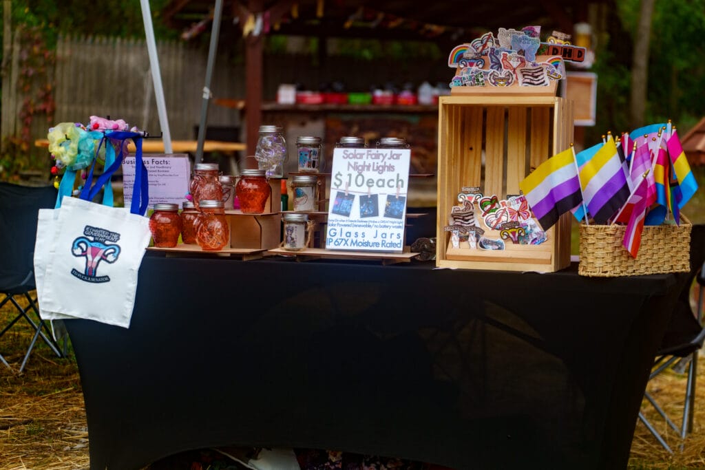 Vendor booth displaying pride flags, stickers, and handmade lantern jars at Lezapalooza.