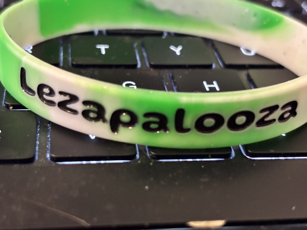 Close-up of a green-and-white wristband with “Lezapalooza” printed in black, resting on a keyboard.
