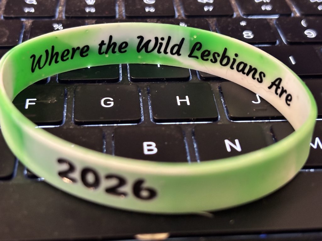 Green-and-white Lezapalooza wristband on a keyboard, showing “Where the Wild Lesbians Are” and “2026.”