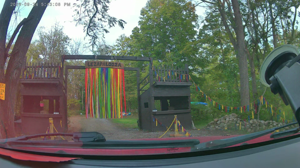 Lezapalooza’s wooden campground gateway with its sign and rainbow ribbon curtain in place, viewed through a windshield.